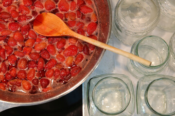 Cooking strawberry jam in a large bowl at home. Wooden spoon in a bowl with jam. Empty glass jars...