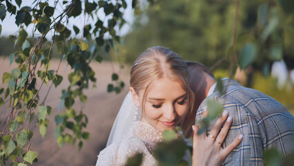 Bride and groom touching and enjoying each other against a backdrop of birch tree branches. - Powered by Adobe