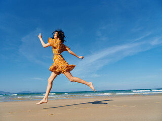 Vibrant woman in flowing yellow dress joyfully running along sandy beach with vibrant blue sky in background
