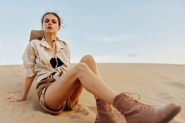 Woman relaxing on top of sand dune with feet buried in sand and enjoying peaceful desert scenery