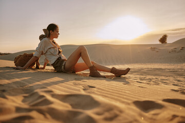 Lonely woman sitting on the sand in the vast desert with her back to the camera, contemplating...