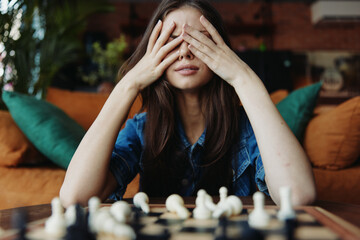 Woman in contemplation, covering her eyes, engrossed in a game of chess on a table