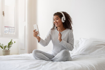 Smiling Young Woman With Headphones Video Calling From Bright Bedroom