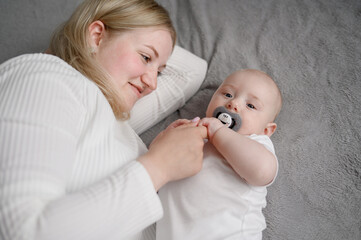 Newborn child with a nipple lies next to her mother on bed, she holds child and, infant feels safe....