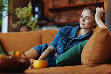 Young woman sitting on couch enjoying a cup of coffee in cozy living room setting