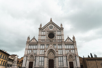 Fototapeta na wymiar Basilica di Santa Croce's Neo-Gothic facade from Piazza di Santa Croce (Florence). Vibrant marble hues adorn three triangular pediments, echoing Florentine architectural tradition, under cloudy sky.