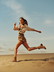 Happy young woman running with arms outstretched in the desert under the bright sun