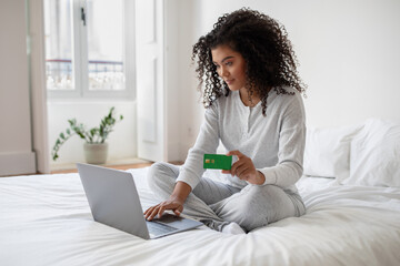 Young Woman Shopping Online With Credit Card in Bright Bedroom