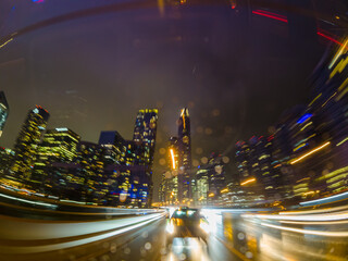 Back car window view of long exposure of the highway in the city. City at night Driving a car, the city at night. Camera at the vehicle back trunk glass. Rainy night soft glowing.