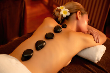 Hot stone massage at spa salon in luxury resort with warm candle light, blissful woman customer...