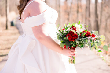 A plus-sized bride is standing outside holding her wedding bouquet.