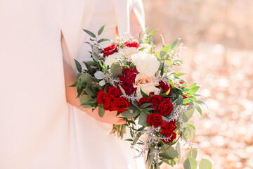 A bride holding a beautiful wedding bouquet of red roses, white flowers, eucalyptus leaves, and greenery