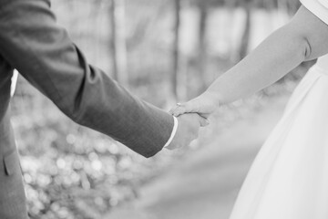 Close-up of bride and groom holding each other's hands, bride is leading groom, in a black and...