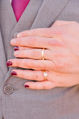 A bride and groom have their hands on the man's vest, showing off their wedding rings.