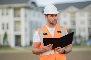 construction inspector in a helmet and construction vest with a clipboard and tablet. male worker...
