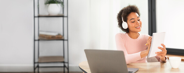 Woman with headphones reading notepad at home