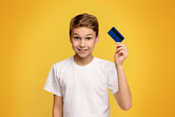 Cute boy holding credit card, orange studio background