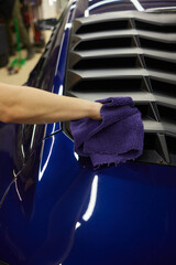 A person is cleaning a blue car with a purple towel