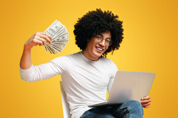 Happy guy working on laptop and showing bunch of money