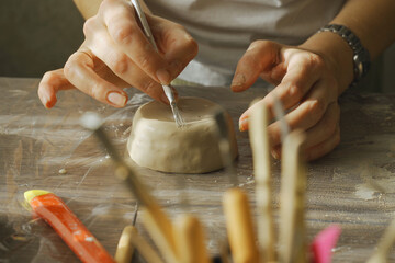 A woman makes a ceramic pot and legs using a tool.