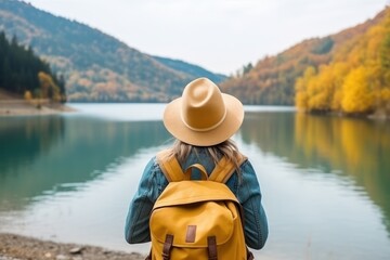 Woman traveler on the shore of a lake in the forest. Concept of travel and adventure in the forest during the autumn season. A woman looks at the beauty of a forest lake. Back view.
