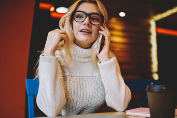 Teen caucasian girl in spectacles calling friend via cellular for conversation during coffee break,...