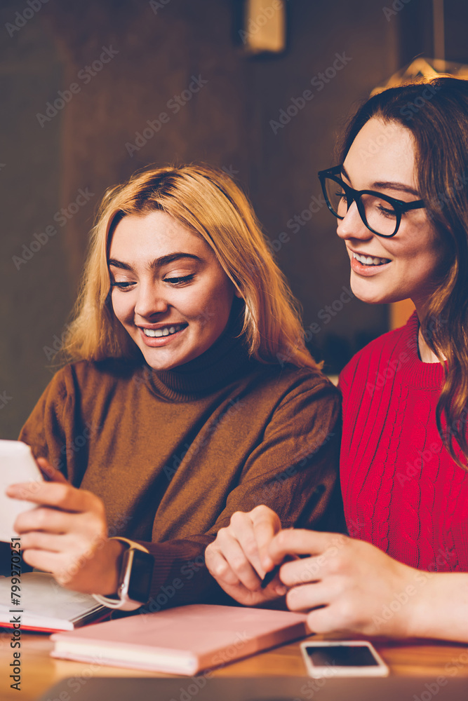Poster smiling hipster girls shopping in web store via portable pc entertaining while learning in coworking