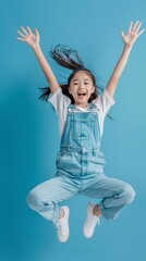 Girl youngster jumping and celebrating in studio with fist in air for goal, achievement, or success on blue background. Young girl, thrilled winner and champion with competition motivation