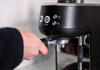 Male hand holding portafilter and making fresh aromatic coffee at home using a modern coffee maker in the kitchen. High quality coffee at home. Business concept with coffee machine.