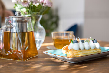 handmade eclairs on a plate, glass teapot with tea on a wooden table, Tea ceremony with cakes on...