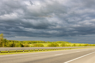 paved road surrounded by fields, against a dramatic sky background.