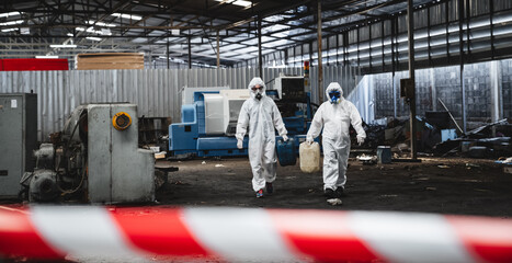 Workers in protective suits inspect chemicals in an old factory, safeguarding against hazards and...