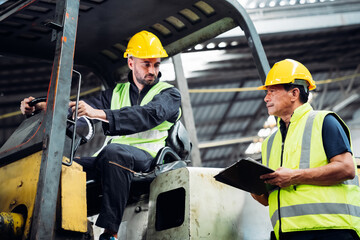 Two men in yellow safety vests are standing next to a forklift