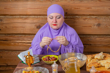 A Muslim woman in a lilac hijab is fingering her rosary at the table, praying for the end of...