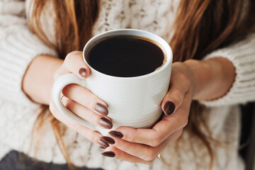Hot coffee in a mug. Woman holding mug of dark coffee. Cold winter relax background. Woolen sweater...