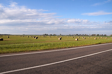 Rural landscape road near a field with hay rolls
