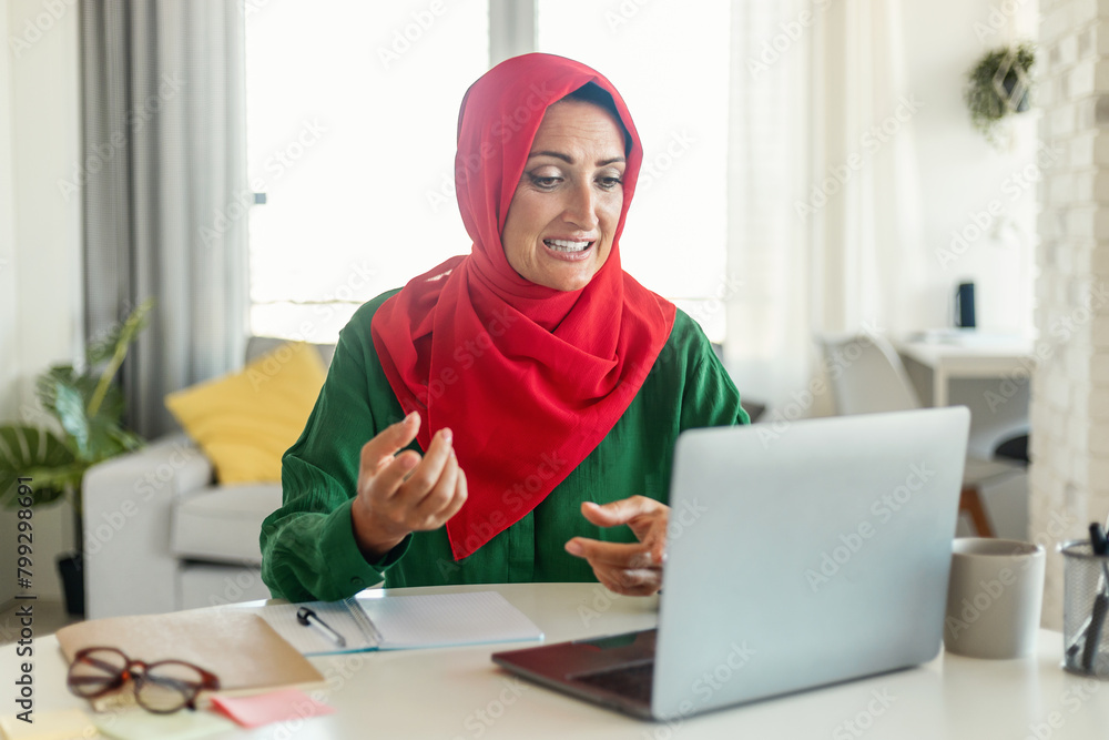 Poster woman in hijab sitting at table using laptop computer