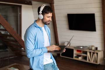 Man Using Laptop Computer With Headphones at Home Interior
