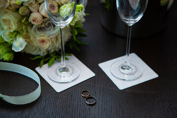 Wedding rings, two champagne glasses, a bouquet on a dark brown table