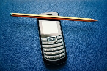 A close-up photo of a classic flip phone with a pencil sticking out from between the casing and the...