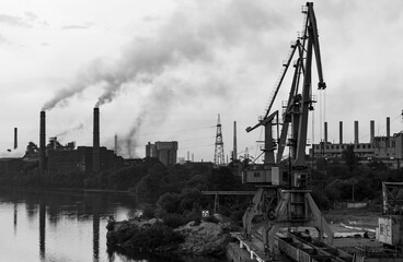 Fototapeta na wymiar Yellow and blue port cranes on the riverbank against the background of the metallurgical plant. Black and white photo