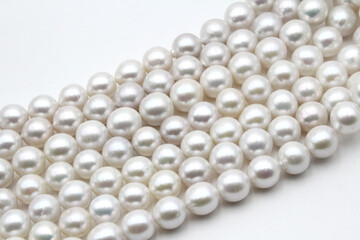 Chinese round freshwater white pearls on strands ready to become a necklace, some of the favorite materials for jewelry on white background. An organic gem that brides love for weddings.