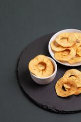 Apple chips in a white plates on a blackstone desk on a dark background.