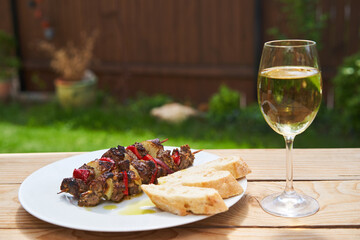 Simple but delicious dish from mediterranean cuisine, Souvlaki skewer from lamb meat and vegetables like paprika and onion served outside in the garden with rusic wheat bread and glass of greek wine.