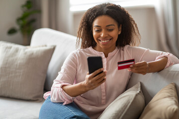 Positive black lady with credit card and phone at home