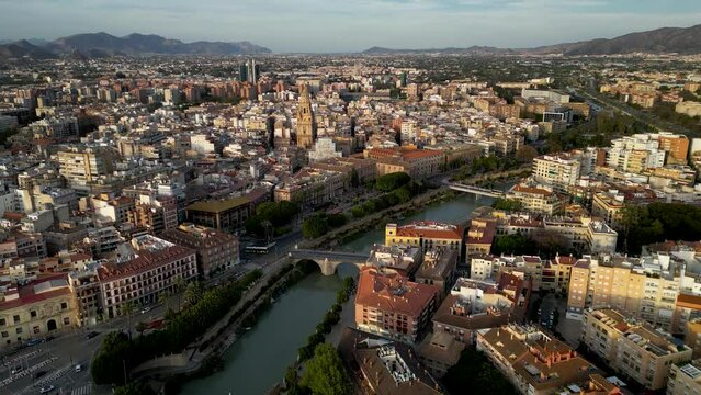 Aerial view of Murcia city, Spain. Panoramic view of all region. Drone descending close to promenade of River Segura. In background is the city center and Cathedral of Murcia. Sunset point. Travel.