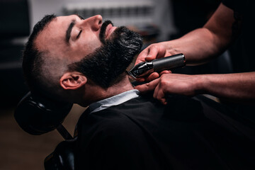 Close-up of a man reclining in his seat having his beard trimmed with an electric razor.