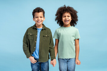 Happy two kids posing in studio while holding hands, looking at camera, smiling