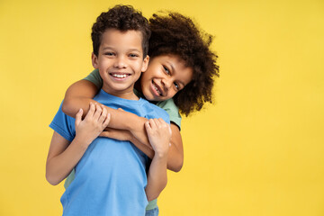 Smiling little girl hugging her brother while posing in studio and looking at camera