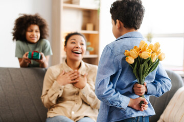 Son holding a bouquet of flowers behind his back as a surprise to his mom, girl holding gift at home
